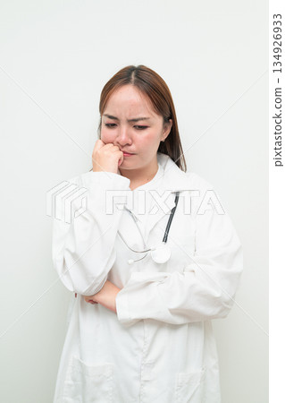 Portrait of young Asian female doctor against white background hand on chin thinking 134926933