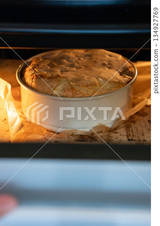 Apple charlotte cake rises in a round baking pan inside the oven, showing golden crust, parchment edges, and warm baking light Apple charlotte cake rises in a round baking pan inside the oven, showing golden crust, parchment edges, and warm baking light 134927769