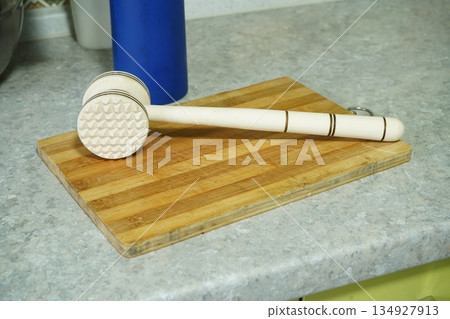 Wooden meat mallet lies on a kitchen board 134927913