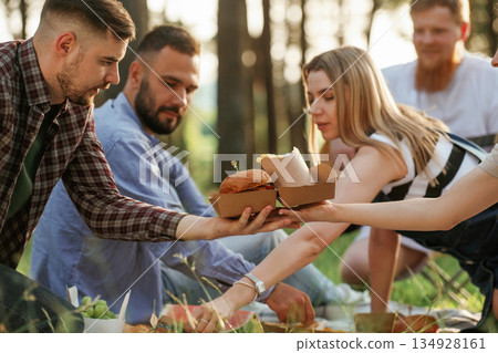 Yummy meal, sitting. Group of friends are having picnic on the field with food in eco boxes 134928161