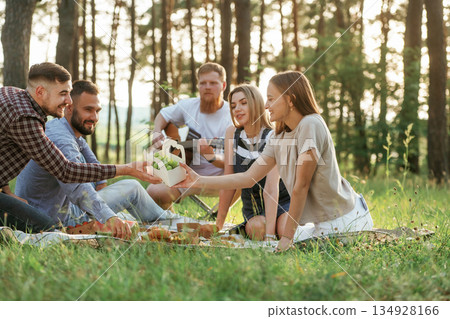 Summertime bonding. Group of friends are having picnic on the field with food in eco boxes Summertime bonding. Group of friends are having picnic on the field with food in eco boxes 134928166