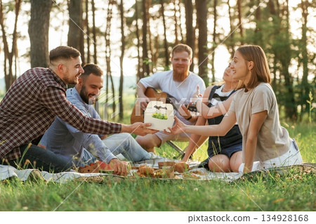 On the ground. Group of friends are having picnic on the field with food in eco boxes 134928168