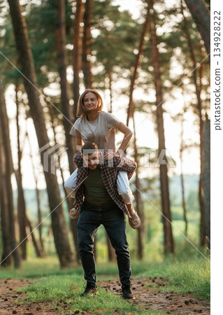 Woman is sitting on the man's back. Lovely couple are together in the forest at summer daytime 134928222