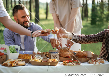 Close up view. Group of friends are having picnic on the field with food in eco boxes Close up view. Group of friends are having picnic on the field with food in eco boxes 134928259