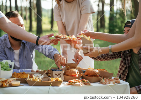 Close up view. Group of friends are having picnic on the field with food in eco boxes Close up view. Group of friends are having picnic on the field with food in eco boxes 134928260
