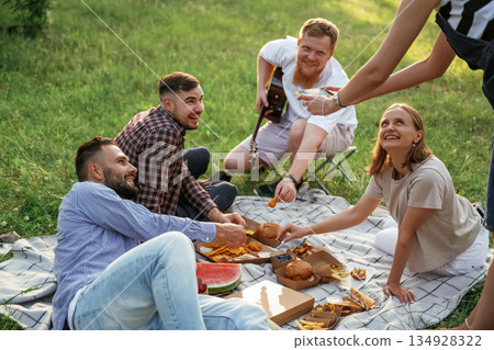 Positive mood, having fun. Group of friends are having picnic on the field with food in eco boxes Positive mood, having fun. Group of friends are having picnic on the field with food in eco boxes 134928322