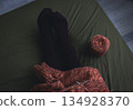 Melange brown sweater with knitting needles and women legs in velvet socks on dark green background. Knitting needles and balls of warm melange yarn. Girl legs and knitting work in process.  134928370