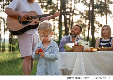 Little boy is with strawberry. Group of friends are having picnic on the field with food in eco boxes 134928397