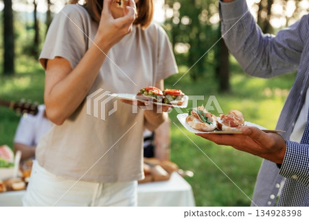 Tasty meal in hands. Group of friends are having picnic on the field with food in eco boxes Tasty meal in hands. Group of friends are having picnic on the field with food in eco boxes 134928398