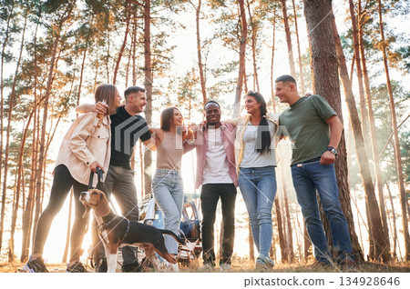 Standing, fun with dog. Group of friends are together in the forest Standing, fun with dog. Group of friends are together in the forest 134928646