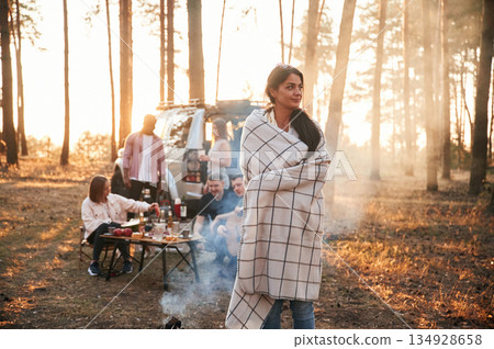 Woman in blanket, standing by bonfire with smoke. Group of friends are together in the forest Woman in blanket, standing by bonfire with smoke. Group of friends are together in the forest 134928658