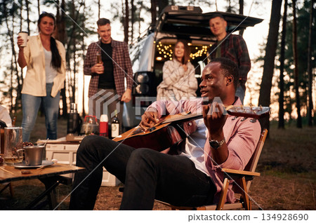 Acoustic guitar player. Group of friends are together in the forest Acoustic guitar player. Group of friends are together in the forest 134928690