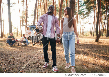 Couple are holding each other by the hands, walking. Group of friends are together in the forest Couple are holding each other by the hands, walking. Group of friends are together in the forest 134928802