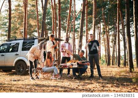 Drinking, eating, playing with dog. Group of friends are together in the forest 134928831