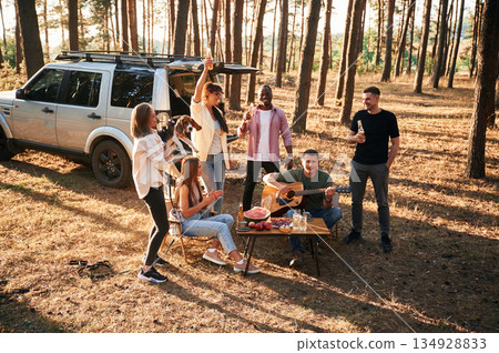 Drinking, eating, playing with dog. Group of friends are together in the forest Drinking, eating, playing with dog. Group of friends are together in the forest 134928833