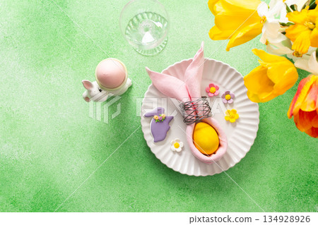 A beautifully arranged Easter table setting showcases a decorative egg nestled in a pink napkin, surrounded by a glass of water and fresh flowers, perfect for holiday gatherings 134928926