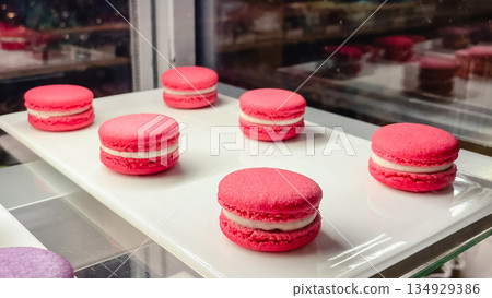 Delicious pink french macarons with white cream filling arranged on a white tray in a bakery Delicious pink french macarons with white cream filling arranged on a white tray in a bakery 134929386