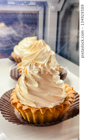 Delicious tartlets topped with elegant swirls of white meringue and golden sprinkles in a bakery display Delicious tartlets topped with elegant swirls of white meringue and golden sprinkles in a bakery display 134929389