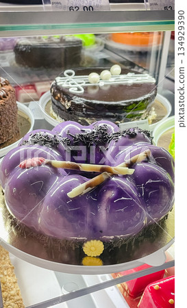 Elegant purple mirror glaze mousse cake with chocolate decorations on display in a bakery showcase Elegant purple mirror glaze mousse cake with chocolate decorations on display in a bakery showcase 134929390