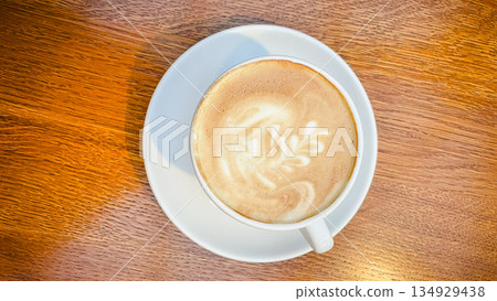 Top view of a white cup of hot cappuccino with beautiful latte art on a natural wooden table surface Top view of a white cup of hot cappuccino with beautiful latte art on a natural wooden table surface 134929438