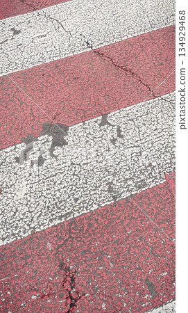Close-up texture of a worn red and white zebra pedestrian crossing on a cracked asphalt road 134929468