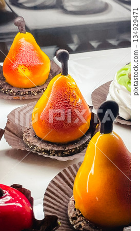 Creative pear-shaped mousse cakes with vibrant orange mirror glaze on a chocolate biscuit base. Creative pear-shaped mousse cakes with vibrant orange mirror glaze on a chocolate biscuit base. 134929471