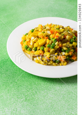 A hearty salad combines boiled egg, tender chicken breast, and vibrant vegetables like potatoes, carrots, and green peas, all dressed with rich olive oil for a nutritious meal 134929843