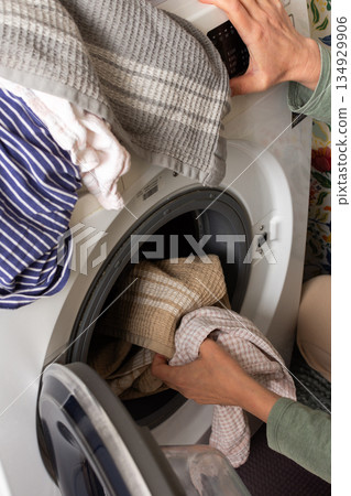 A person is loading freshly sorted laundry into a washing machine. The setting is a cozy home environment with a colorful background. The task is part of a regular cleaning routine 134929906