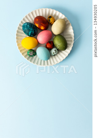 A variety of decorated Easter eggs in vibrant colors are creatively arranged on a white plate set against a soft blue background, symbolizing spring festivities and joy 134930205