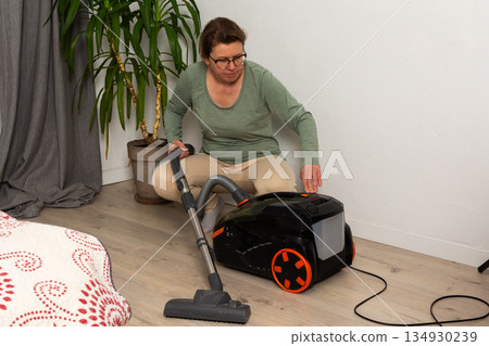Person is getting a vacuum cleaner ready for use in a living room. The vacuum is plugged in and they are holding the hose, preparing to clean the floor 134930239