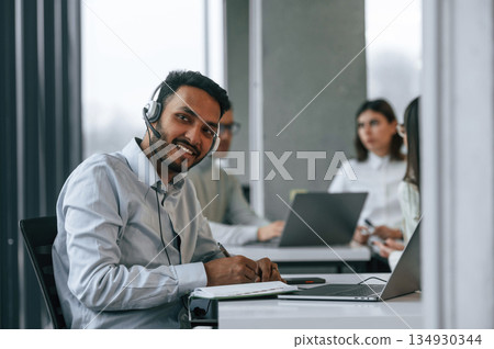 Man is sitting in front of his colleagues. Four people are working in the office together Man is sitting in front of his colleagues. Four people are working in the office together 134930344