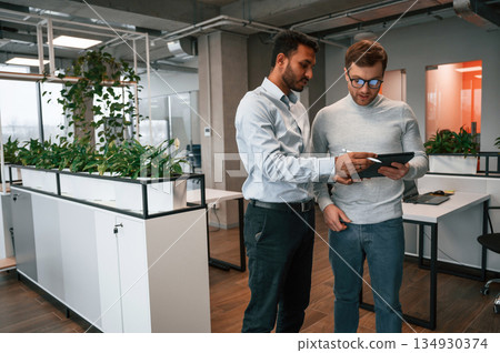 Information in the tablet. Two men are working in the modern office together Information in the tablet. Two men are working in the modern office together 134930374