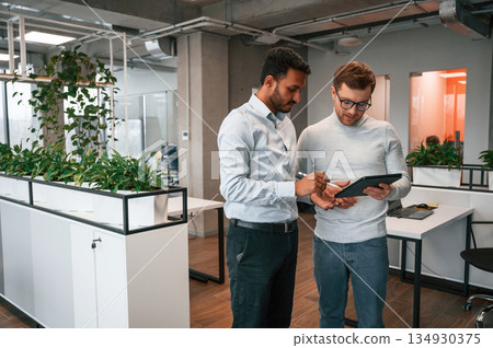 Information in the tablet. Two men are working in the modern office together Information in the tablet. Two men are working in the modern office together 134930375