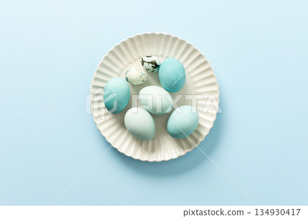 A collection of decorated blue Easter eggs sits on a white plate, showcasing various shades and patterns. The light background enhances the festive atmosphere of Easter 134930417