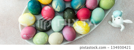 Multi-colored Easter eggs in an oval dish with decorative bunnies, top view Multi-colored Easter eggs in an oval dish with decorative bunnies, top view 134930421