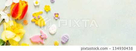 Bright tulips and daffodils surround playful Easter cookies and candies, showcasing the vibrant spirit of springtime festivities and holiday celebrations, banner 134930438