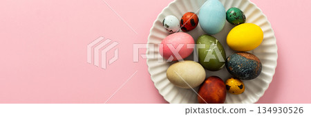 A variety of decorated Easter eggs are arranged on a circular plate against a soft pink background, showcasing vibrant colors and intricate designs for a seasonal celebration, banner A variety of decorated Easter eggs are arranged on a circular plate against a soft pink background, showcasing vibrant colors and intricate designs for a seasonal celebration, banner 134930526