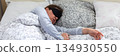 A 50-year-old woman is peacefully sleeping in a cozy bed. She wears a sleep mask and is snuggled under soft blankets, creating a serene atmosphere for rest, banner 134930550