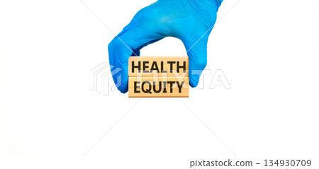 Health equity symbol. Concept words Health equity on beautiful wooden blocks. Doctor's hand in blue medical glove. Beautiful white background. Medical healthy lifestyle health equity concept. Health equity symbol. Concept words Health equity on beautiful wooden blocks. Doctor's hand in blue medical glove. Beautiful white background. Medical healthy lifestyle health equity concept. 134930709