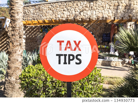 Tax tips symbol. Concept word Tax tips on beautiful red and white road sign. Beautiful palm tree and market background. Business tax tips concept. Copy space. Tax tips symbol. Concept word Tax tips on beautiful red and white road sign. Beautiful palm tree and market background. Business tax tips concept. Copy space. 134930773