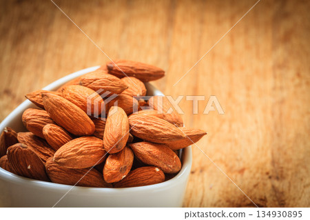 Almonds in bowl on wooden background 134930895