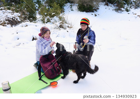 Friends Enjoy A Snowy Winter Picnic With Dog On Snowy Trail 134930923
