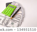 The image features a small, green electronic calculator and a pen on top of US hundred dollar bills. 134931510