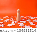 Wooden peg doll surrounded by white jigsaw puzzle pieces on an orange background. 134931514