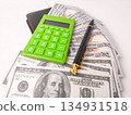 The image features a small, green electronic calculator and a pen on top of US hundred dollar bills. 134931518
