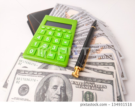 The image features a small, green electronic calculator and a pen on top of US hundred dollar bills. 134931518