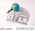 The image displays a small globe and a pen resting on top of a stack of U.S. hundred-dollar bills, symbolizing global finance or international business. 134931519