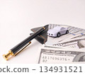 Small toy car model resting on top of US dollar bills and a pen, likely symbolizing financial concepts related to vehicles. 134931521
