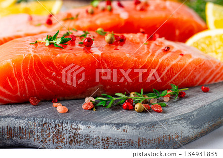 Fresh salmon fillets with herbs and citrus on a wooden cutting board at a kitchen counter ready for cooking 134931835