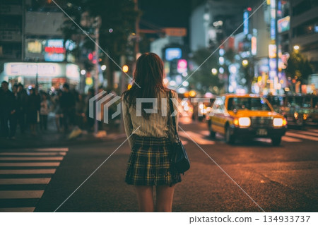 Night Woman Stands at Crosswalk in Busy City Street With Bright Lights and Moving Cars Around Prostitute 134933737